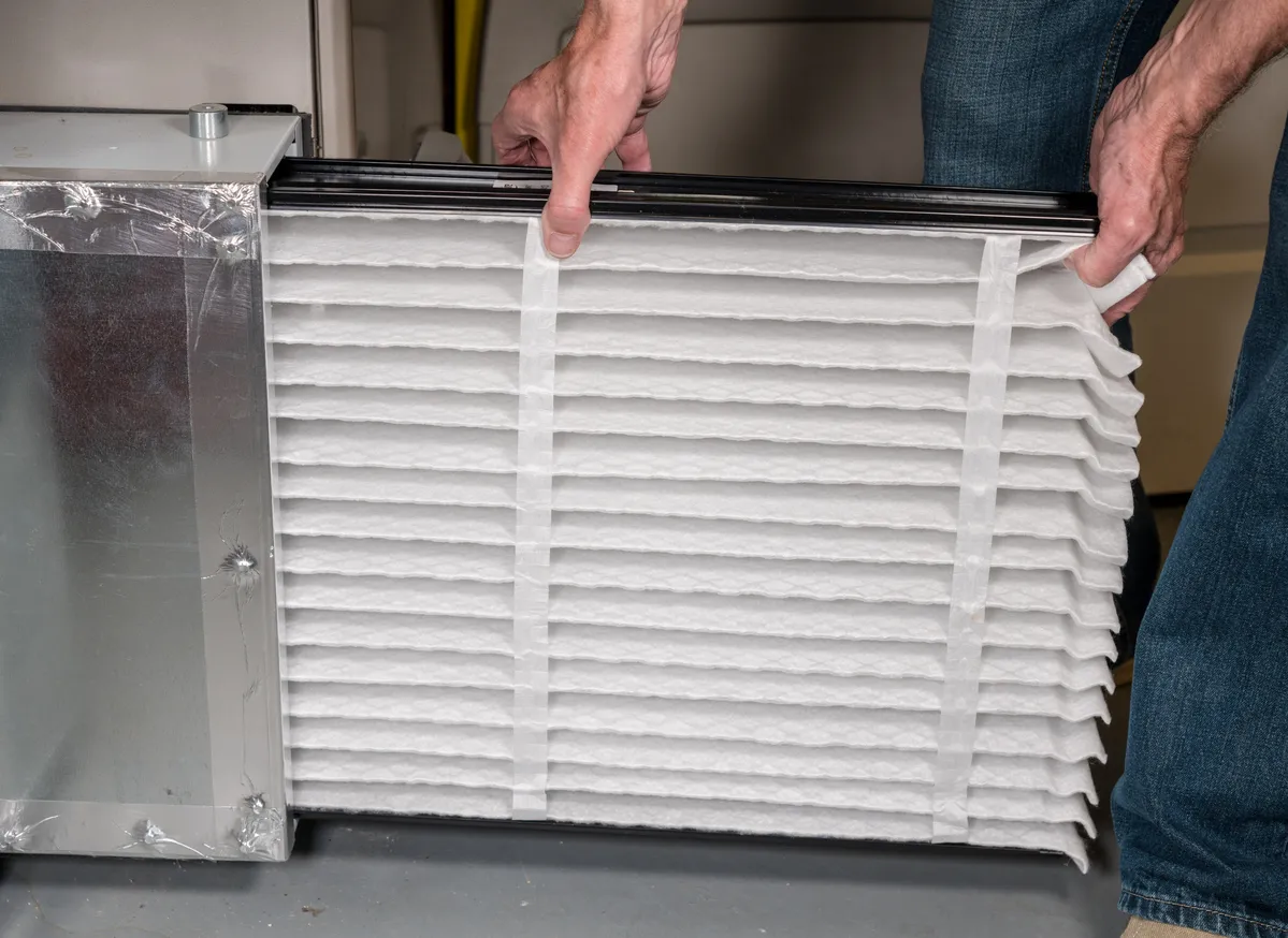 Hombre mayor insertando un nuevo filtro de aire en un horno HVAC