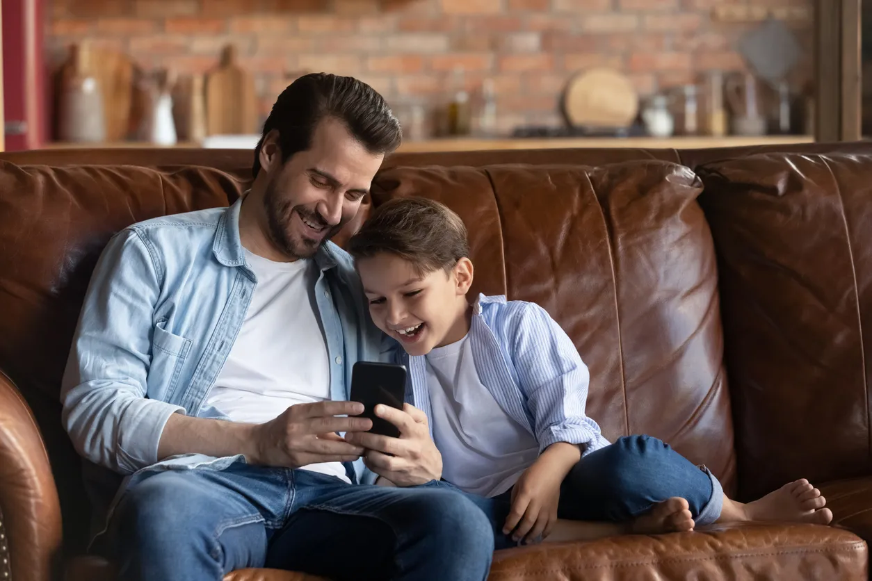 Un niño feliz y su padre usan un teléfono inteligente de media gama en casa
