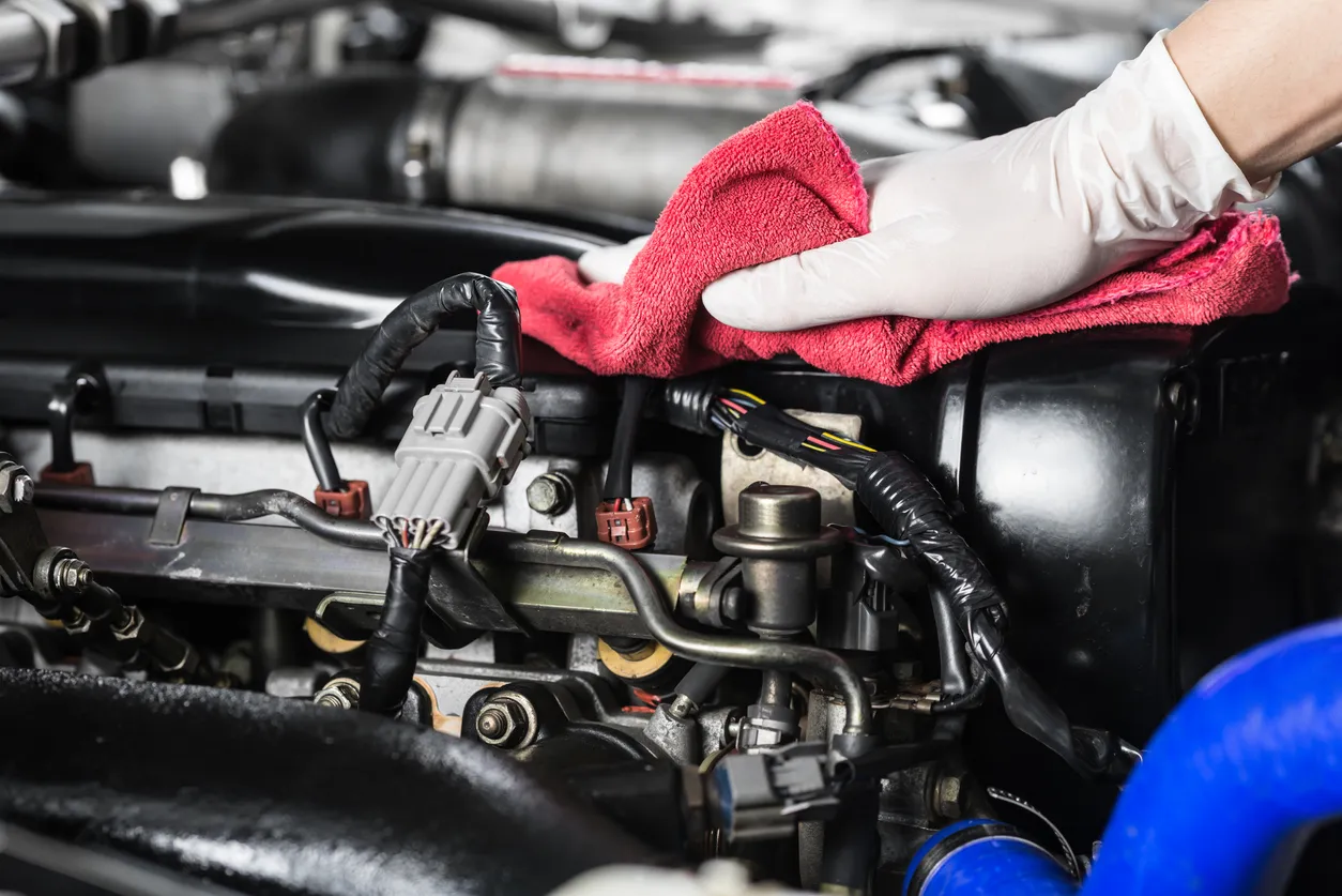 Persona con guante limpiando el motor de un auto. El desengrasante mineral es utilizado para limpiar un motor