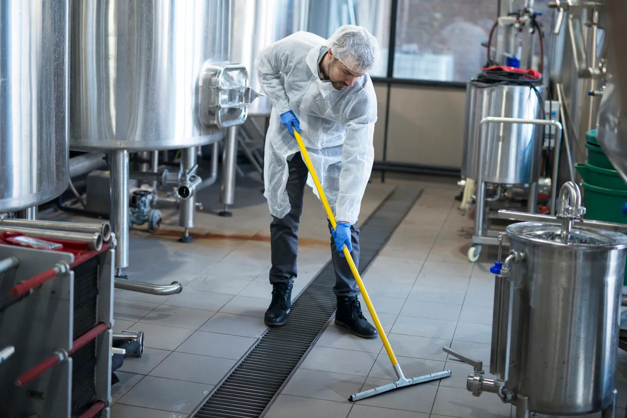 Servicio de limpieza industrial. Limpiador profesional con uniforme de protección para la limpieza del suelo de la planta