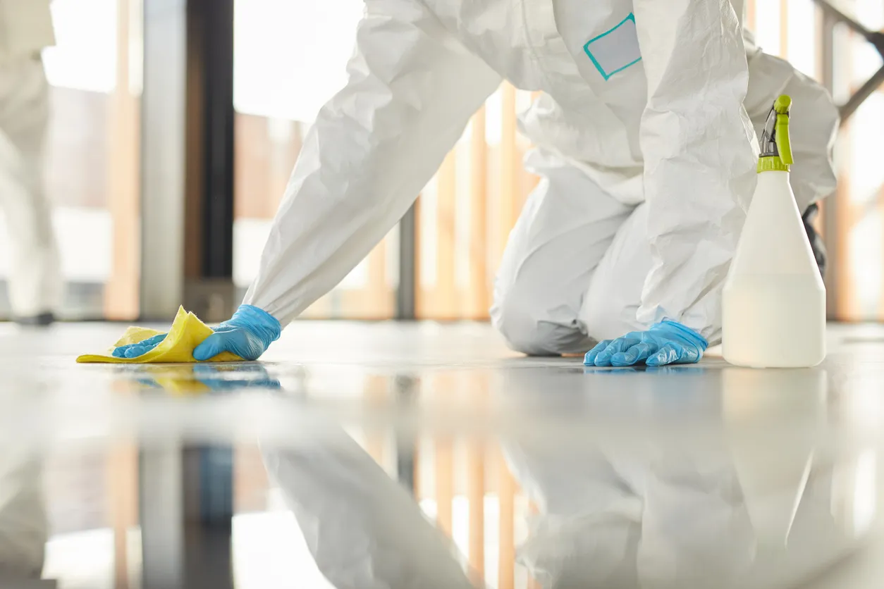Primer plano de un trabajador irreconocible con traje protector limpiando el piso con productos químicos