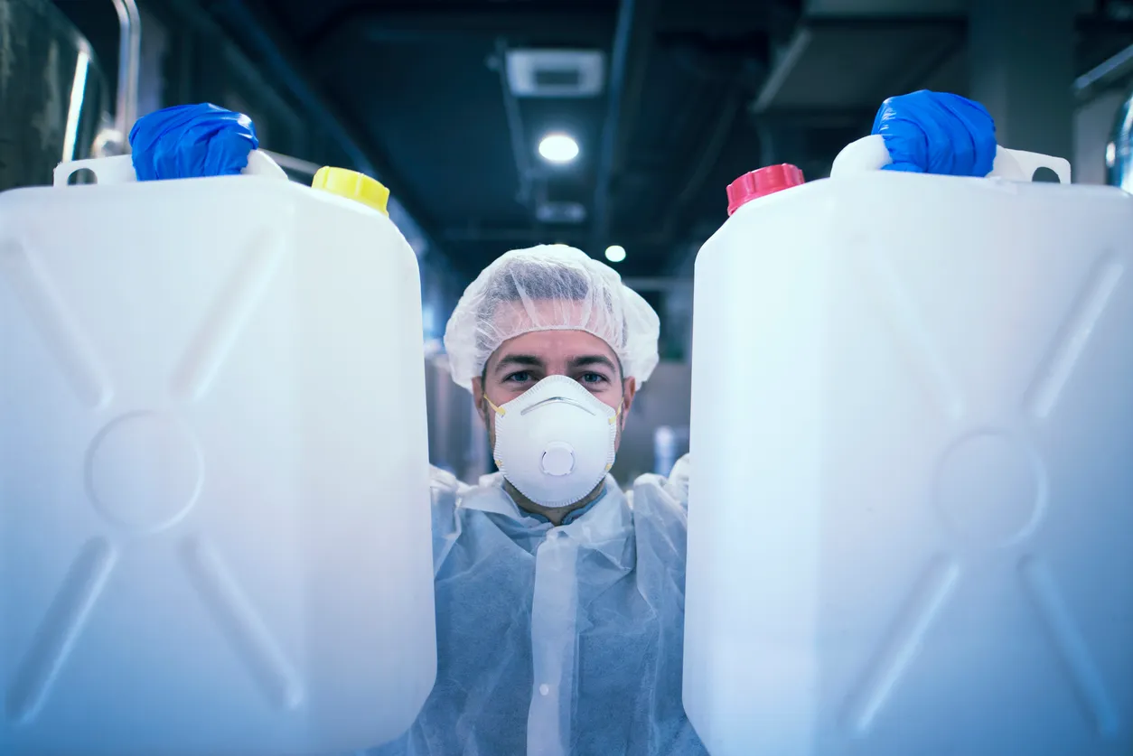 Trabajador industrial con traje de protección sosteniendo botes de plástico con productos de limpieza en fábrica