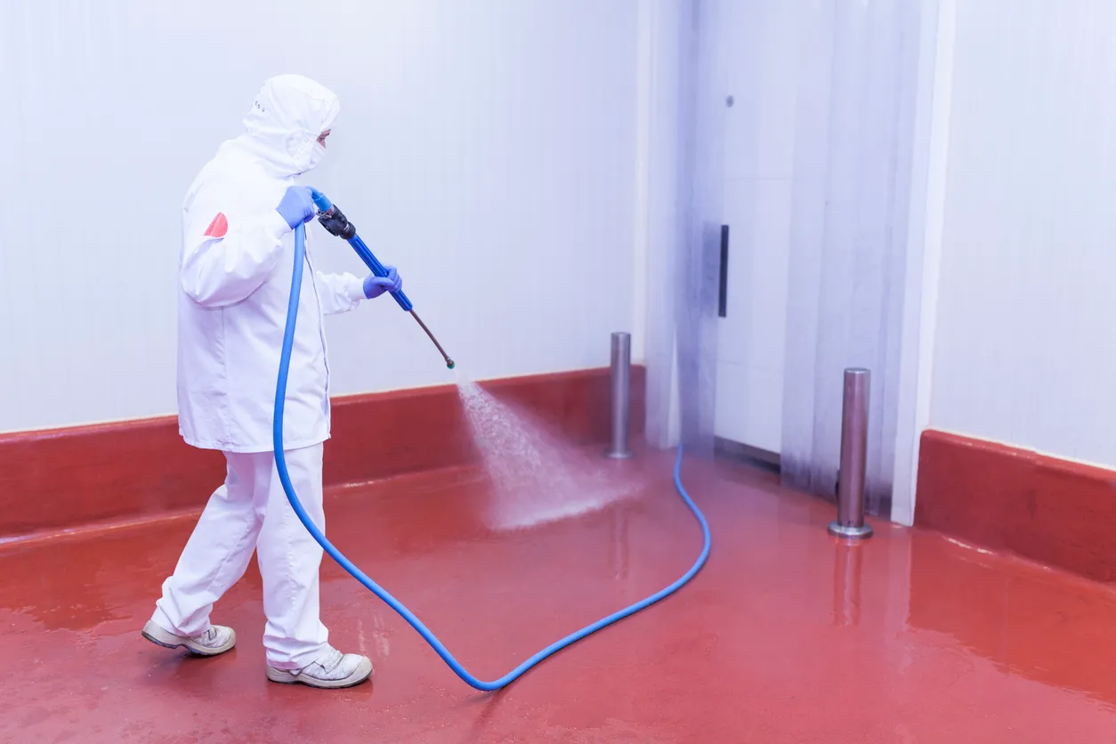 Trabajador de la sala de corte lavando la cámara frigorífica con equipo de presión de agua y vestido con ropa higiénica