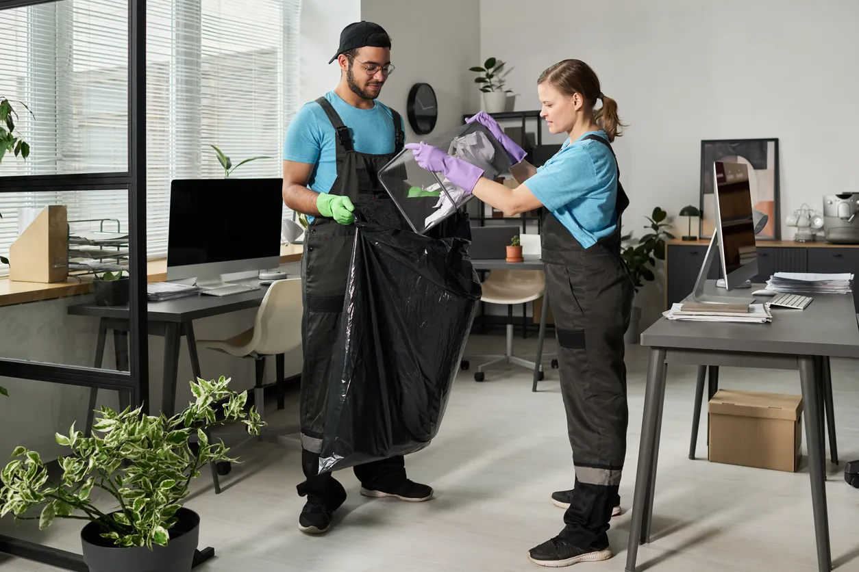 Trabajadores de limpieza tirando basura en bolsas de basura durante la limpieza en la oficina