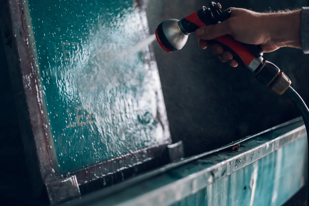 Trabajador masculino limpiando el marco de la pantalla con agua en un taller de impresión