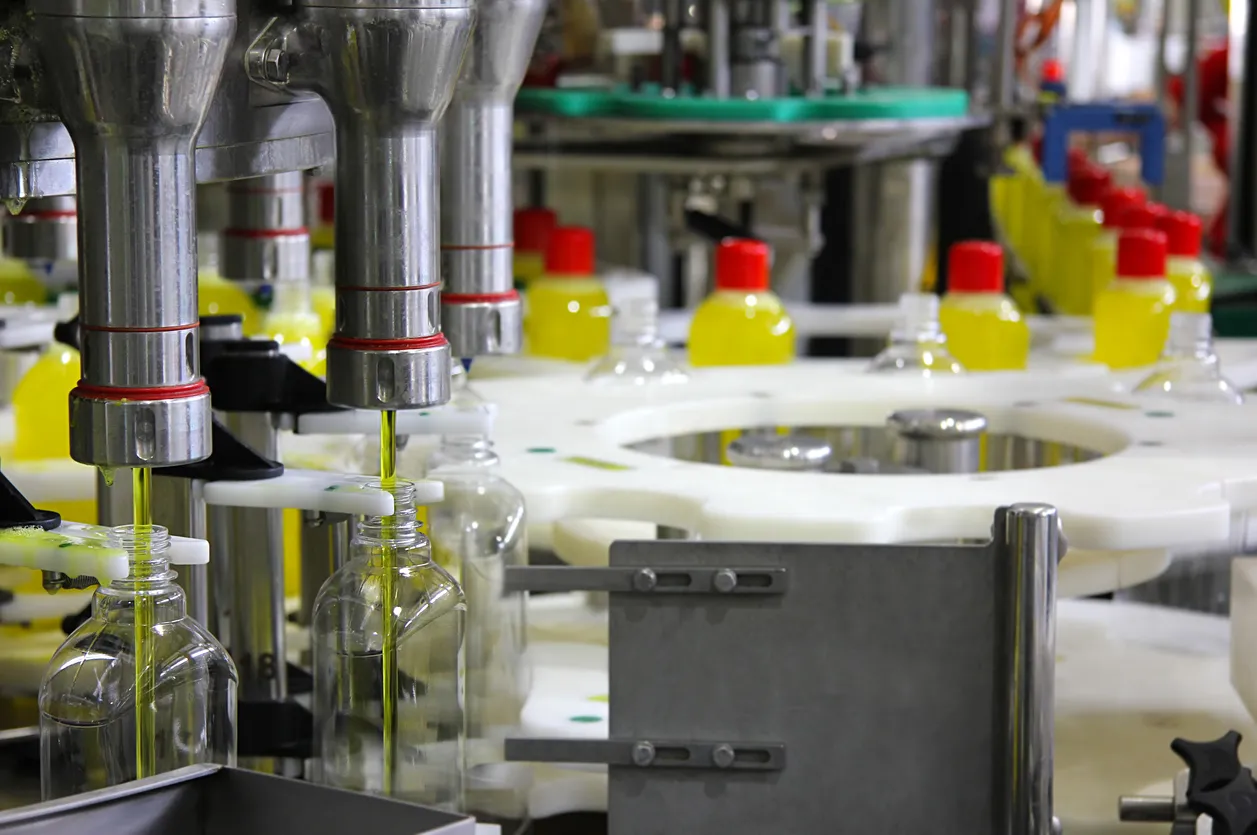 Receipientes de plastico son llenados por una máquina con desengrasante.