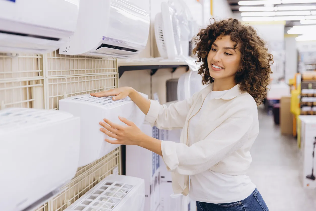 Mujer elige un nuevo aire acondicionado entre varios modelos en una tienda de electrodomésticos luminosa y organizada.