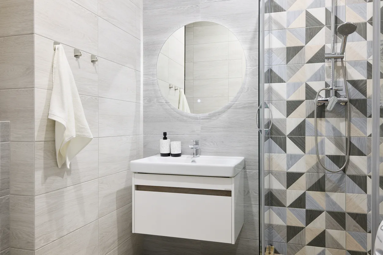 Este elegante baño exhibe hermosos azulejos geométricos, un lavabo rectangular moderno y un impresionante espejo circular.