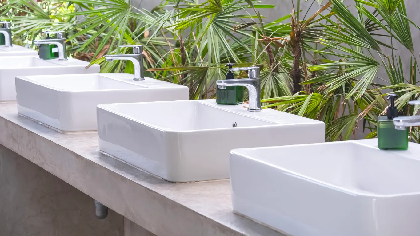 Fila de lavabos de cerámica cuadrados blancos y grifos de acero inoxidable sobre un mostrador de hormigón