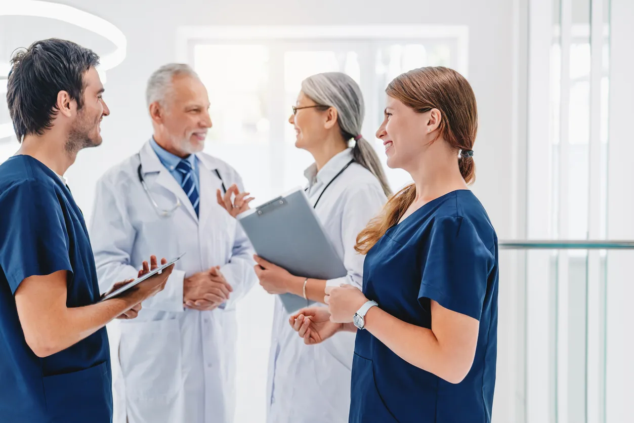 Un equipo de profesionales sanitarios con uniformes azules y blancos conversa en el pasillo del hospital.