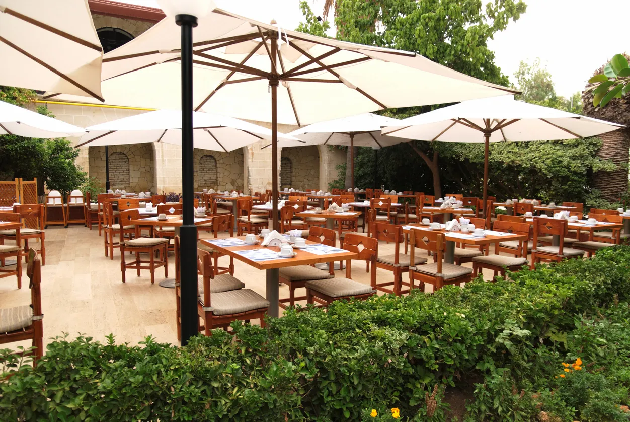 una gran cantidad de mesas y sillas en el exterior de un gran restaurante con jardín alrrededor