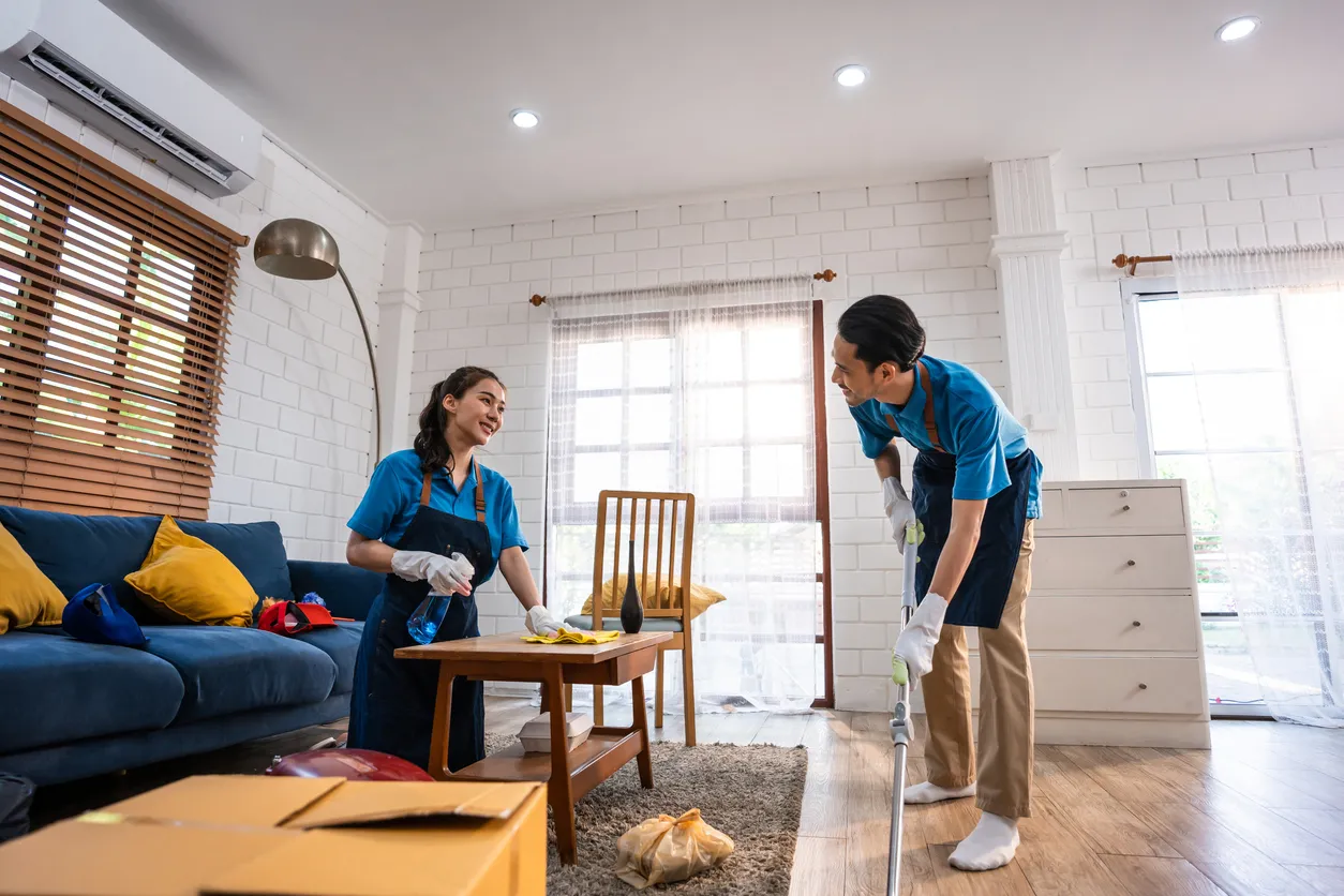 Dos jovenes con uniforme y accesorios de limpieza en la sala de una casa