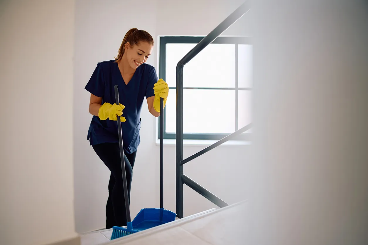 Pesona con uniforme azul y guantes realizando la limpieza de las escaleras de una casa