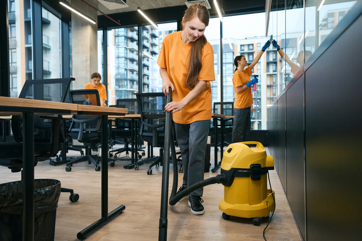 Personas con uniforme de playera naranja y acceosorios de limpieza trabajando en oficinas