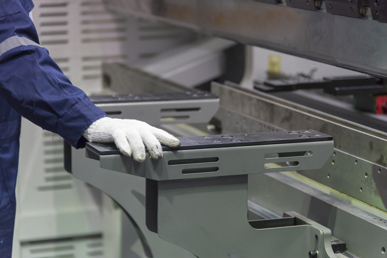 De cerca, el operador de la máquina dobladora sujeta las piezas de chapa metálica con un guante de goma. 