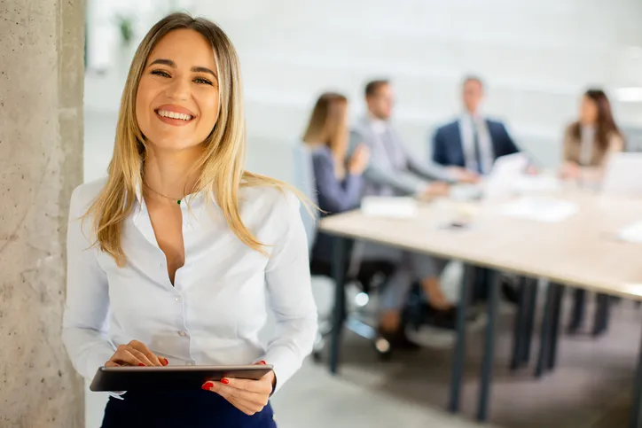 Mujer sonriente en una sala de reuniones con compañaros al fondo