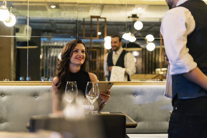 Mesero antendiendo una mujer sentada en la mesa de un restaurante 