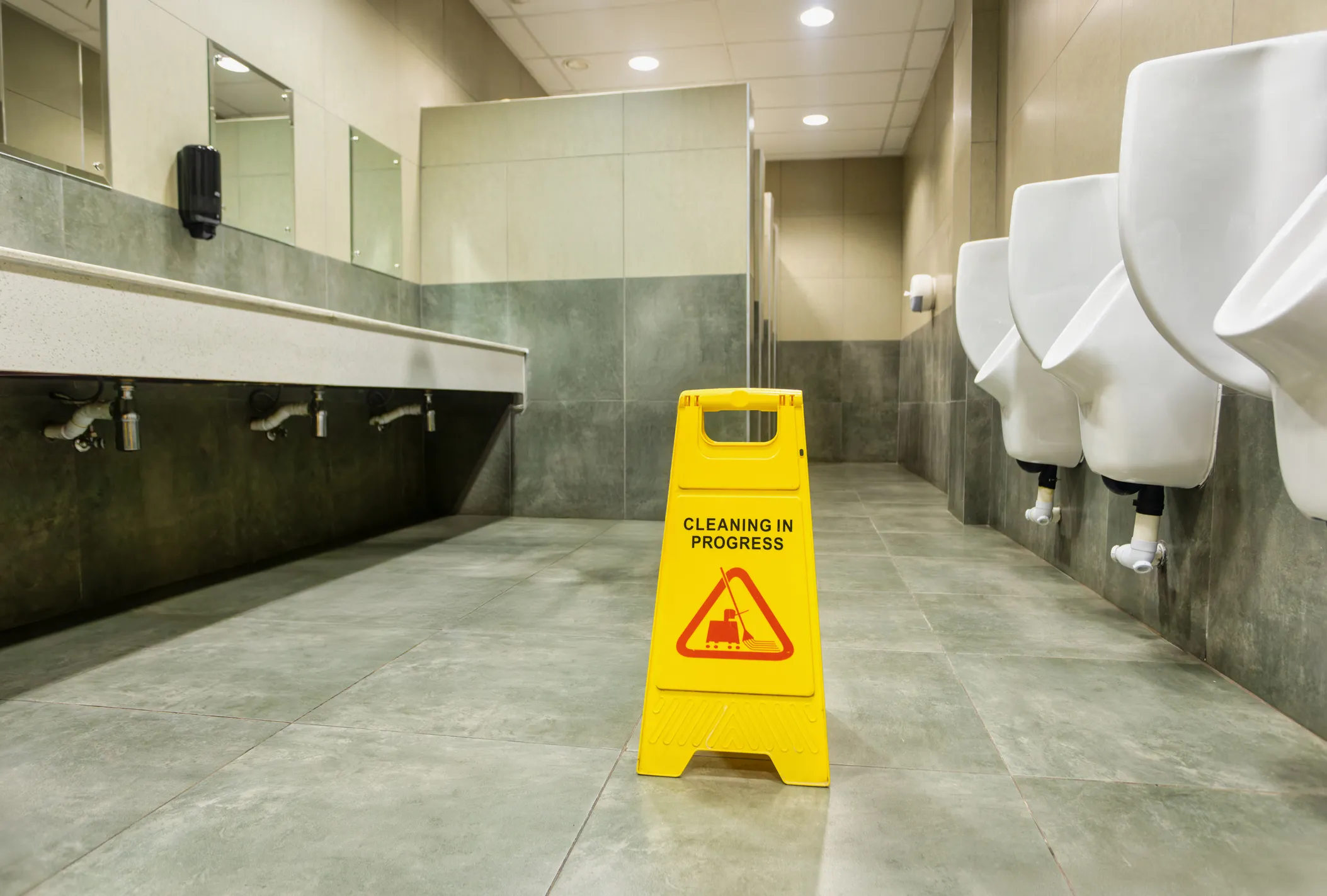 Baños públicos con un letrero amarillo que indica que están en limpieza usando detergentes industriales.