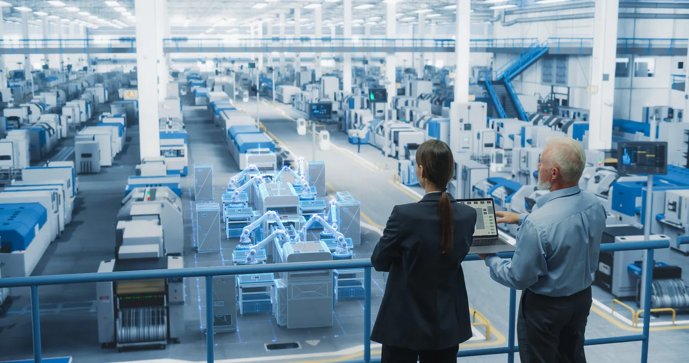Dos personas desde una barandilla observando la producción en una fábrica de electrónicos. 