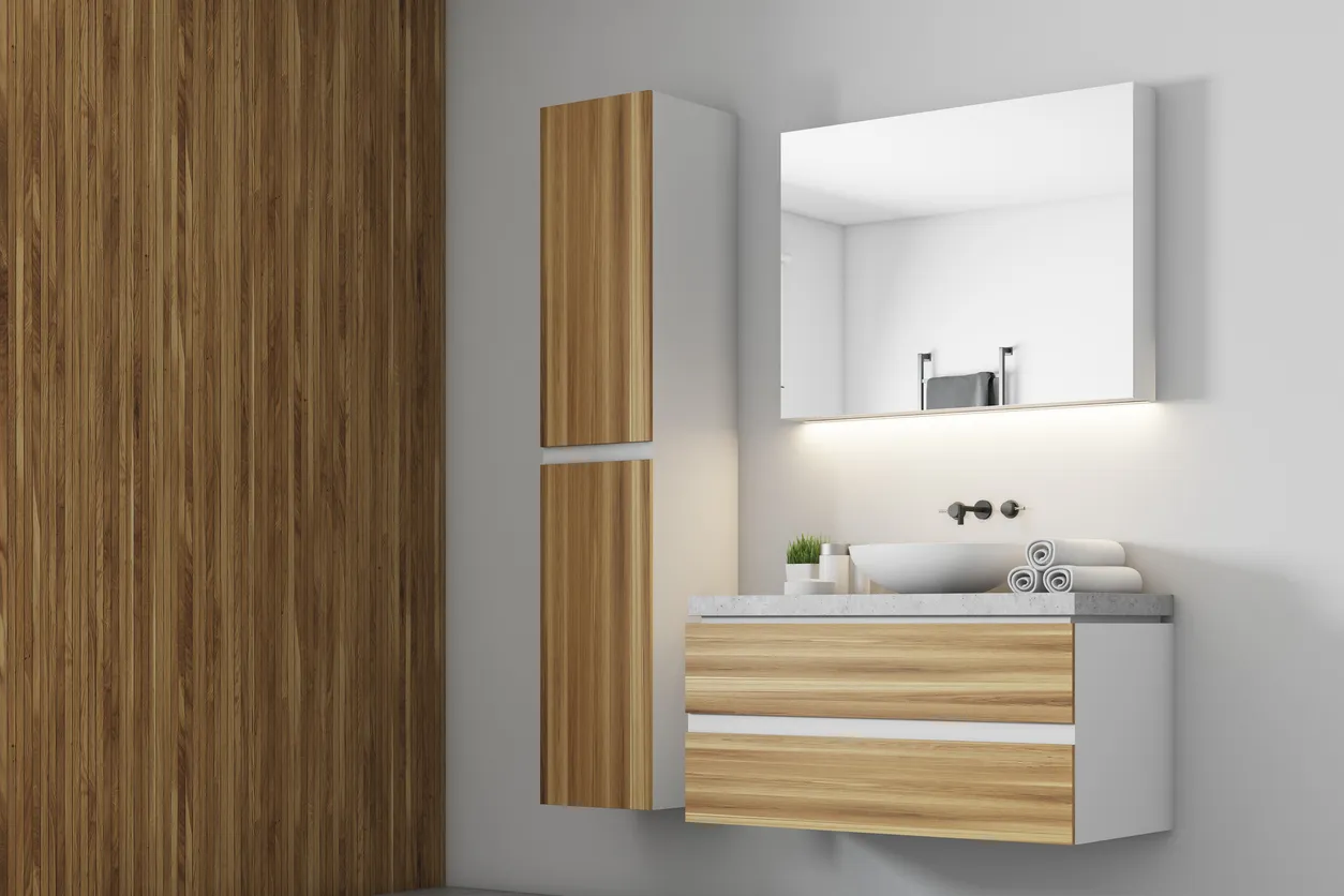 Vista lateral de un lavabo blanco sobre un juego de cajones de madera en un baño blanco con un armario de madera.