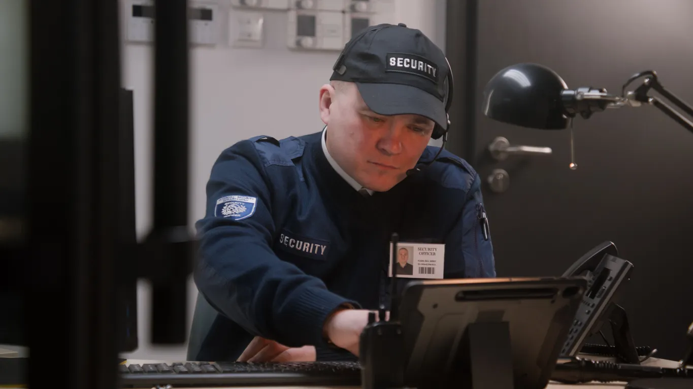 Guardia de seguridad con uniforrme realizando una revisión en su dispositivo de las cámaras instaladas en la empresa