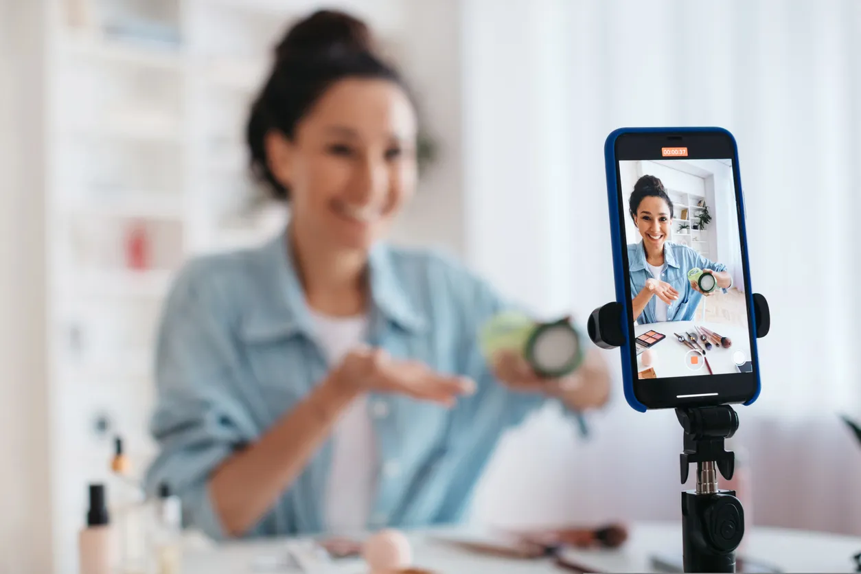 Blogger femenina usando el teléfono mostrando productos de maquillaje haciendo videos en interiores