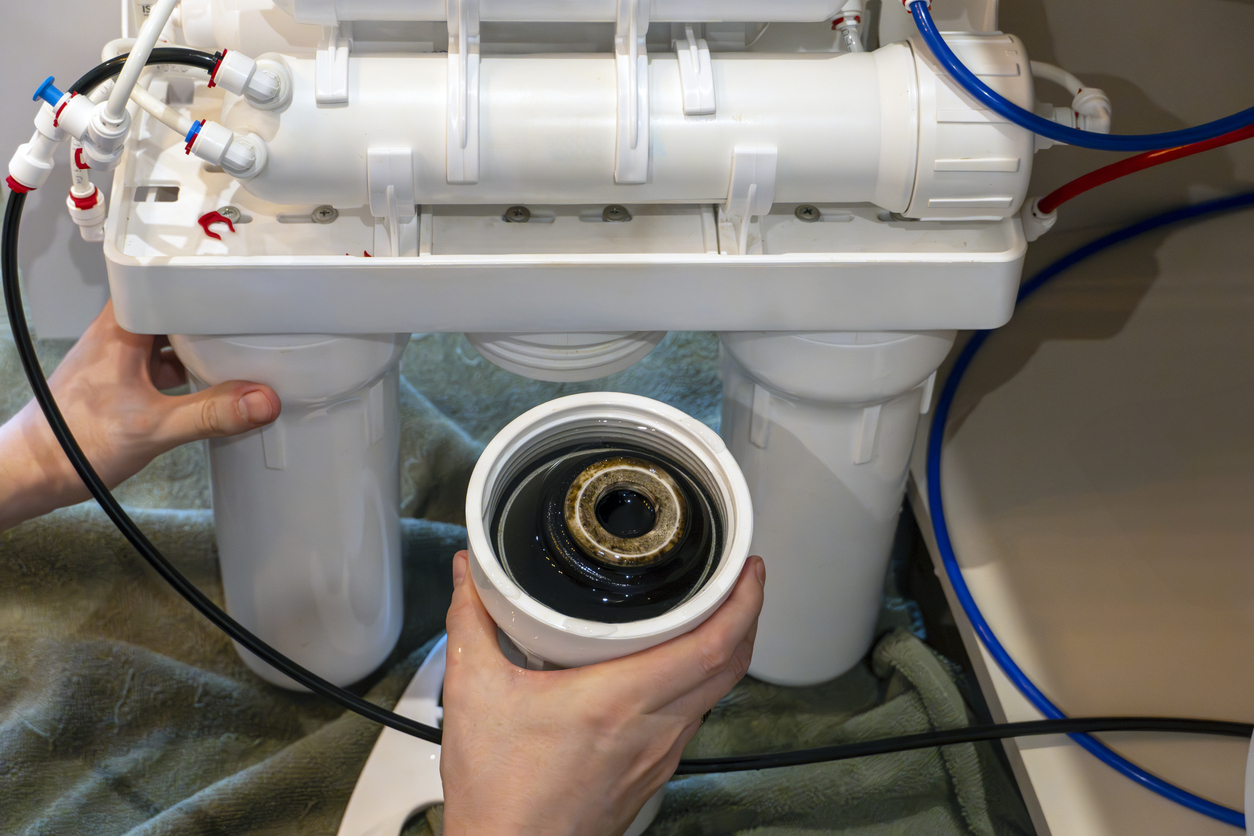 Vista de cerca del cartucho de filtro de agua usada sucia que se retira del sistema de purificación durante el reemplazo de r