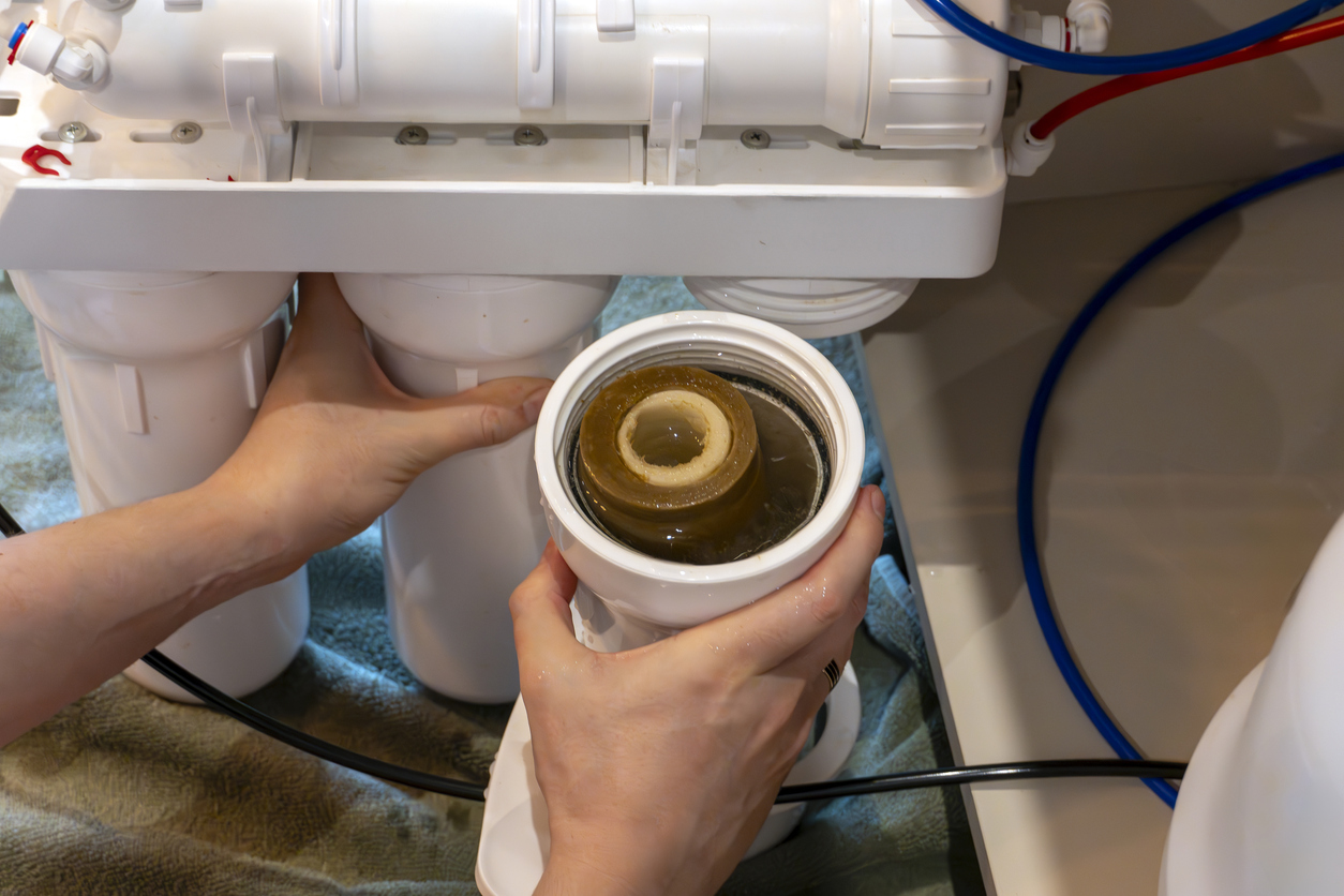 Una persona que realiza el mantenimiento de un sistema de filtro de agua de ósmosis inversa doméstico