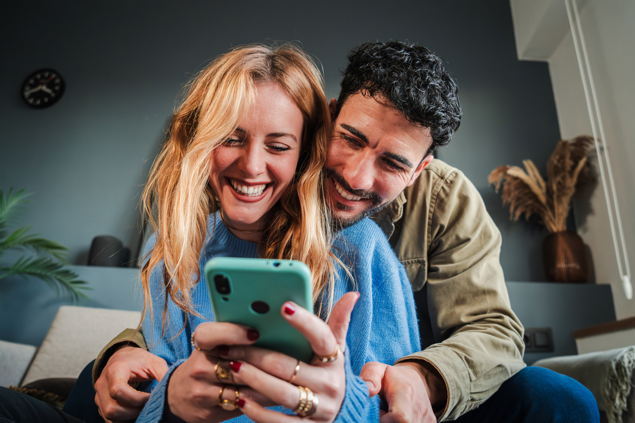 Joven pareja caucásica sonriendo usando un teléfono celular para hacer compras en línea.
