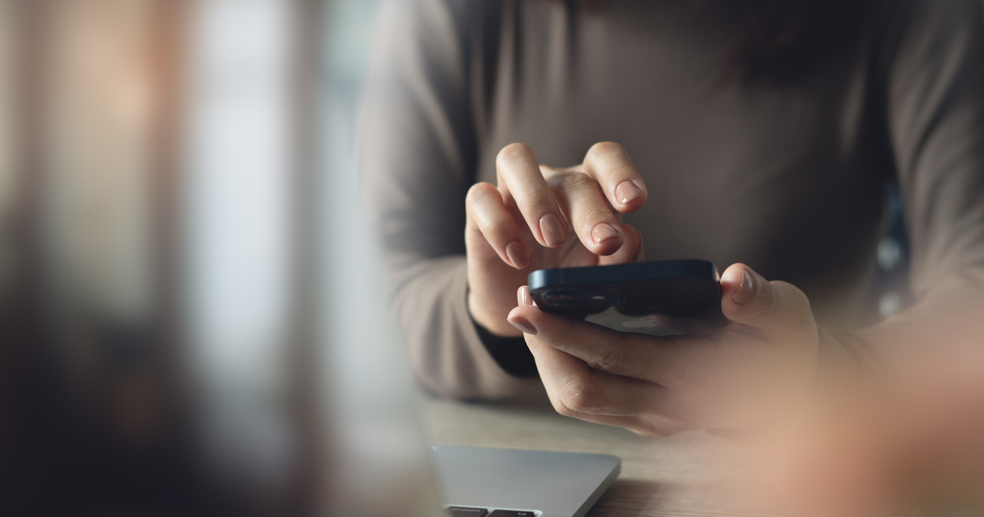 De cerca, mujer de negocios usando el teléfono móvil con la computadora portátil en la mesa de la oficina. 