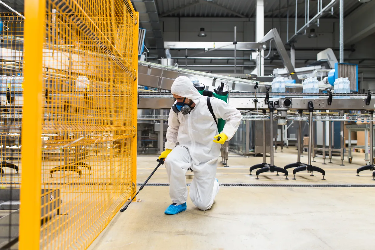 Persona con uniforme completo y mascarilla realizando la fumigación en un gran almacén