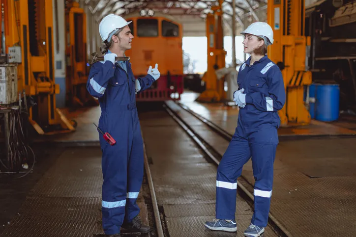 Hombre y mujer con overoles industriales y casco blanco en industria