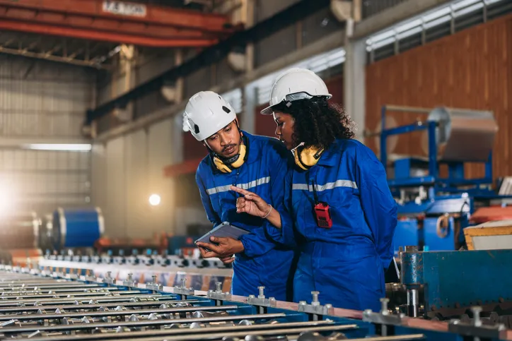 Obreros industriales coon overoles inspeccionando y verificando máquinas en fábrica