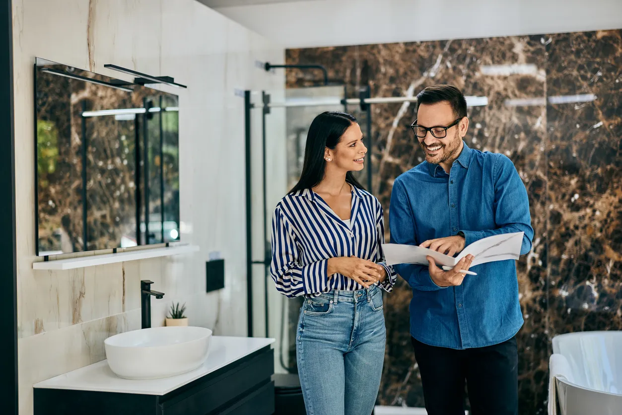 Un vendedor le muetra a una clienta algunas fotos de muebles para baños. Tiendas de muebles para baño cerca de mí.