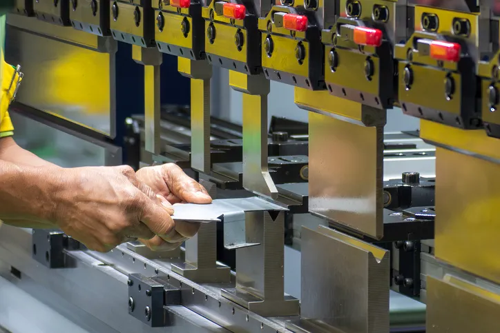 operario de la máquina dobladora sujetando las piezas de chapa metálica
