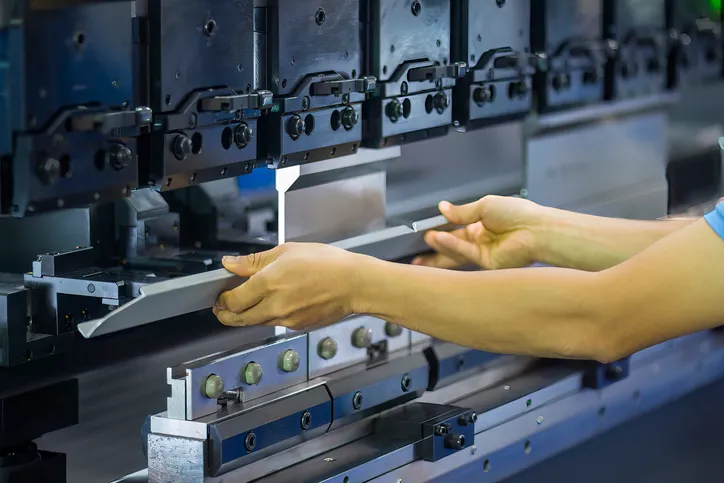 De cerca, el operador de la máquina dobladora sujeta las piezas de chapa. 