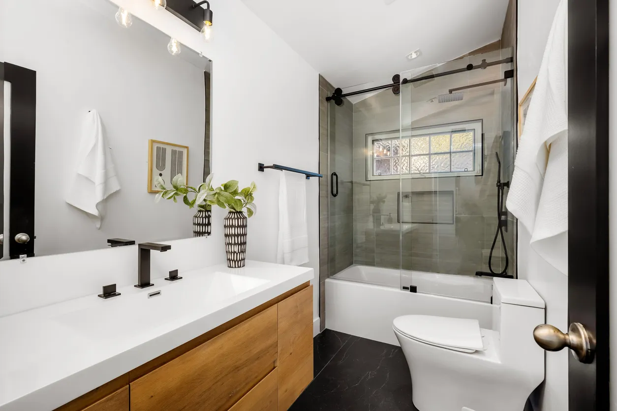 Baños pequeños elegante. Tocador de madera con lavabo blanco y al fondo una tina de baño pequeña.