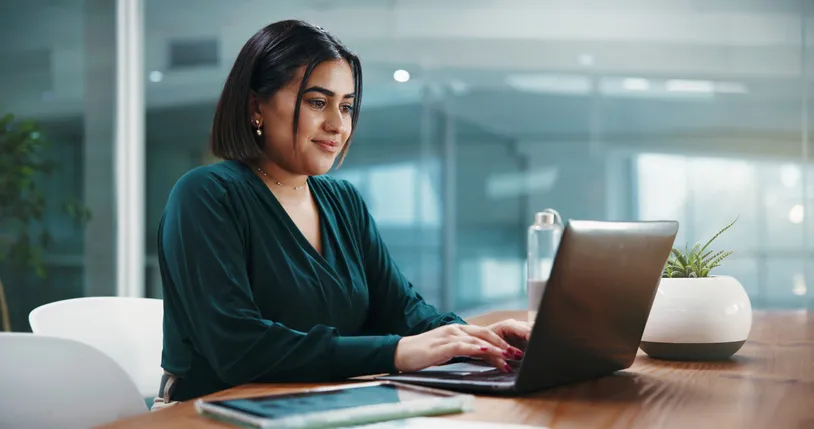 mujer joven sentada frente a un escritorio utilizando una laptop
