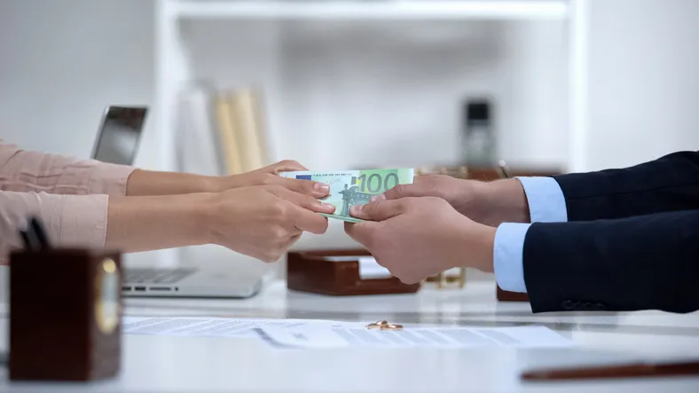 Se visualizan dos pares de manos extendidas, una entregando dinero a la otra.persona