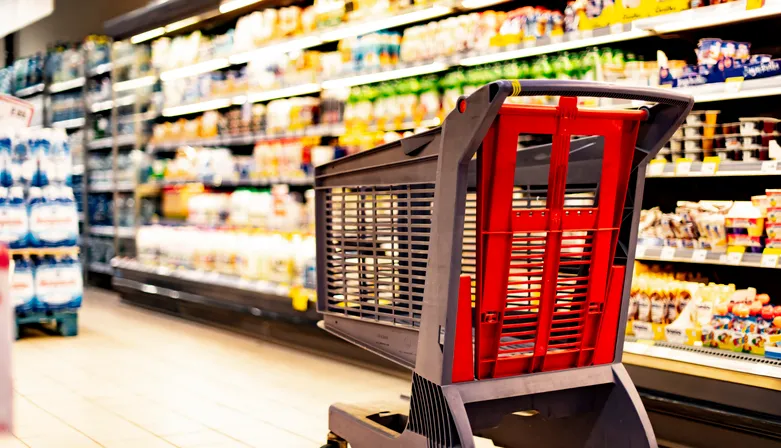 Un carrito de compras junto a un estante de una tienda en un supermercado 