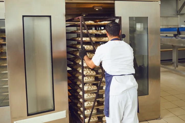 El panadero empuja una bandeja con pan del horno en la panadería.