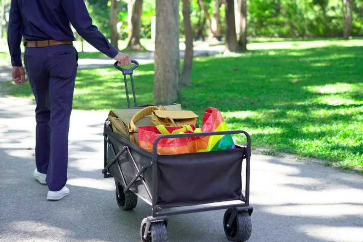 Hombre caminando tirando de carrito plegable con cosar