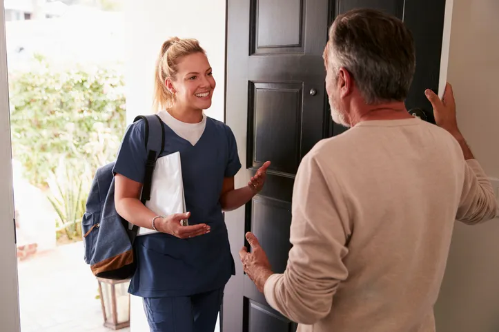 Hombre abrd su puerta de entrada a una trabajadora de salud haciendo un salud en el hogar,