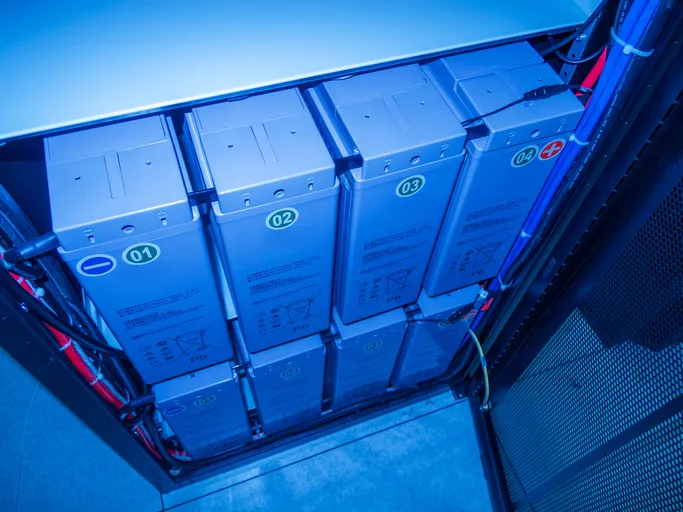 Esta imagen muestra una sala de servidores moderna con unidades de almacenamiento de baterías iluminadas con luz azul,