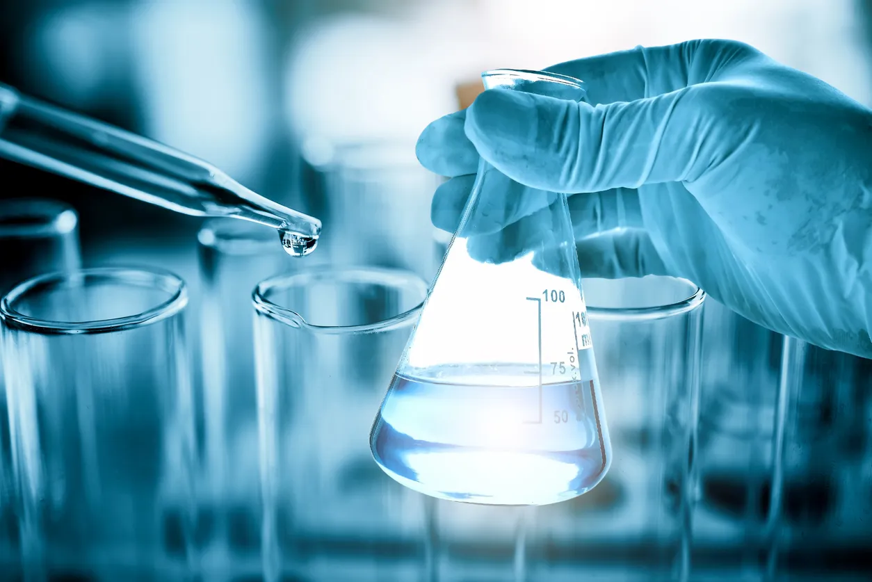 Mano de científico con matraz de vidrio fondo de laboratorio químico.El agua bidestilada es utilizada para preparar reactivos