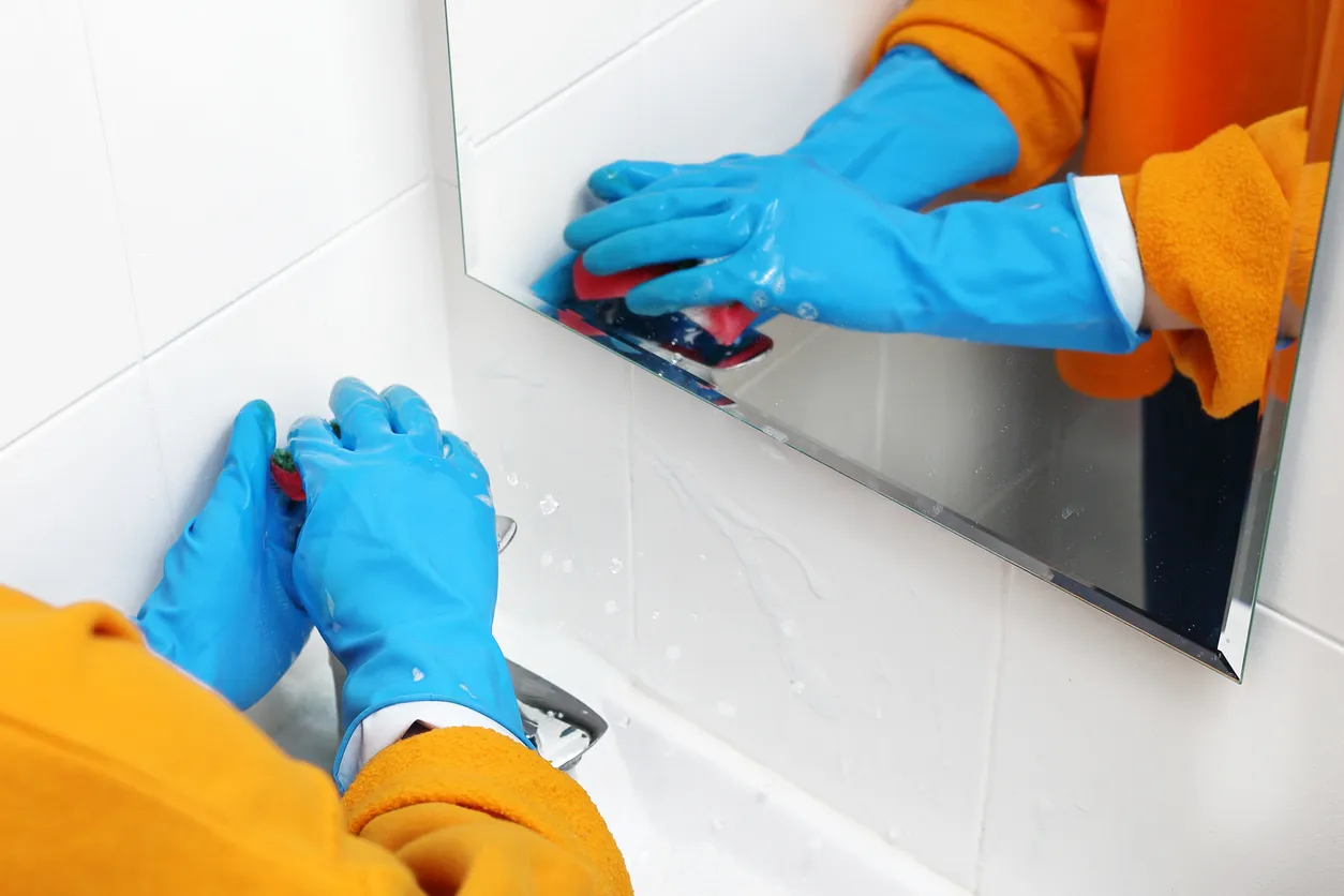 manos de persona con guantes lavando el lavabo de un baño