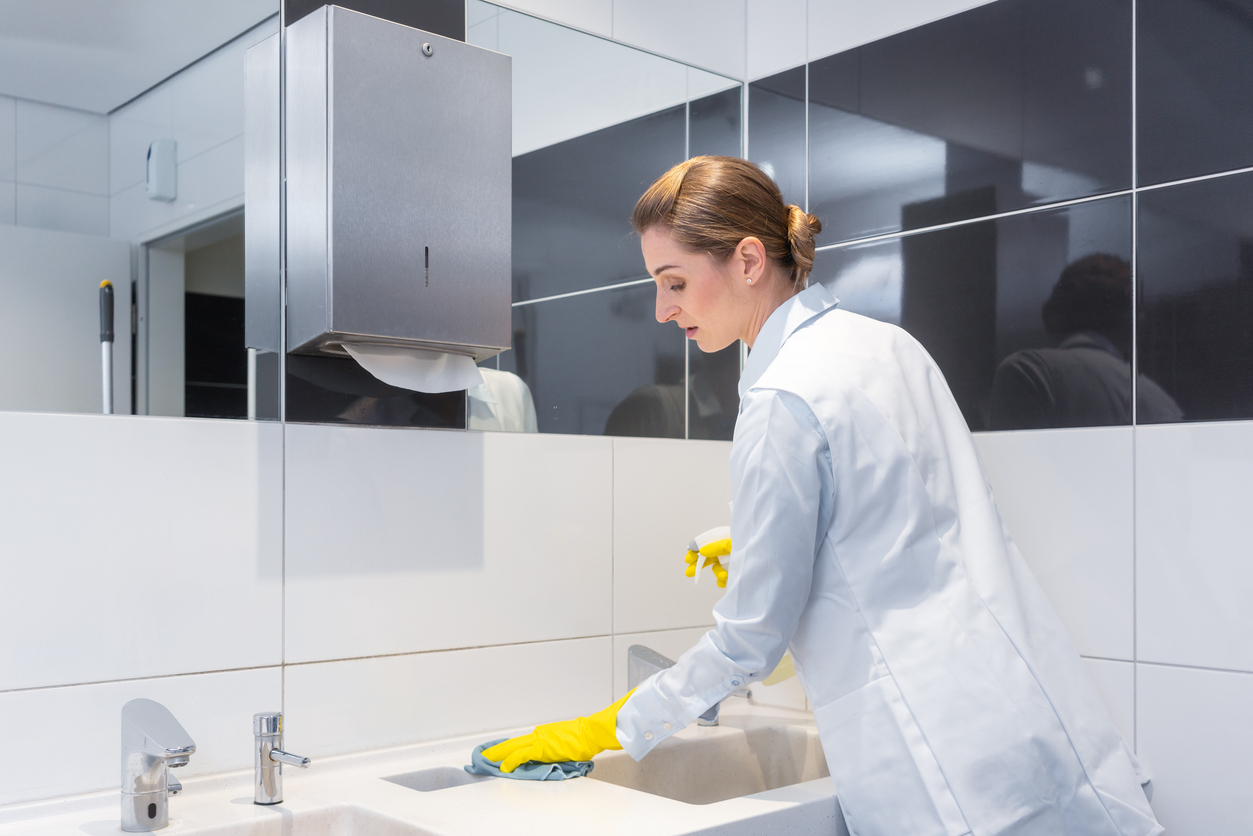 Mujer limpiando un lavabo de un baño público 