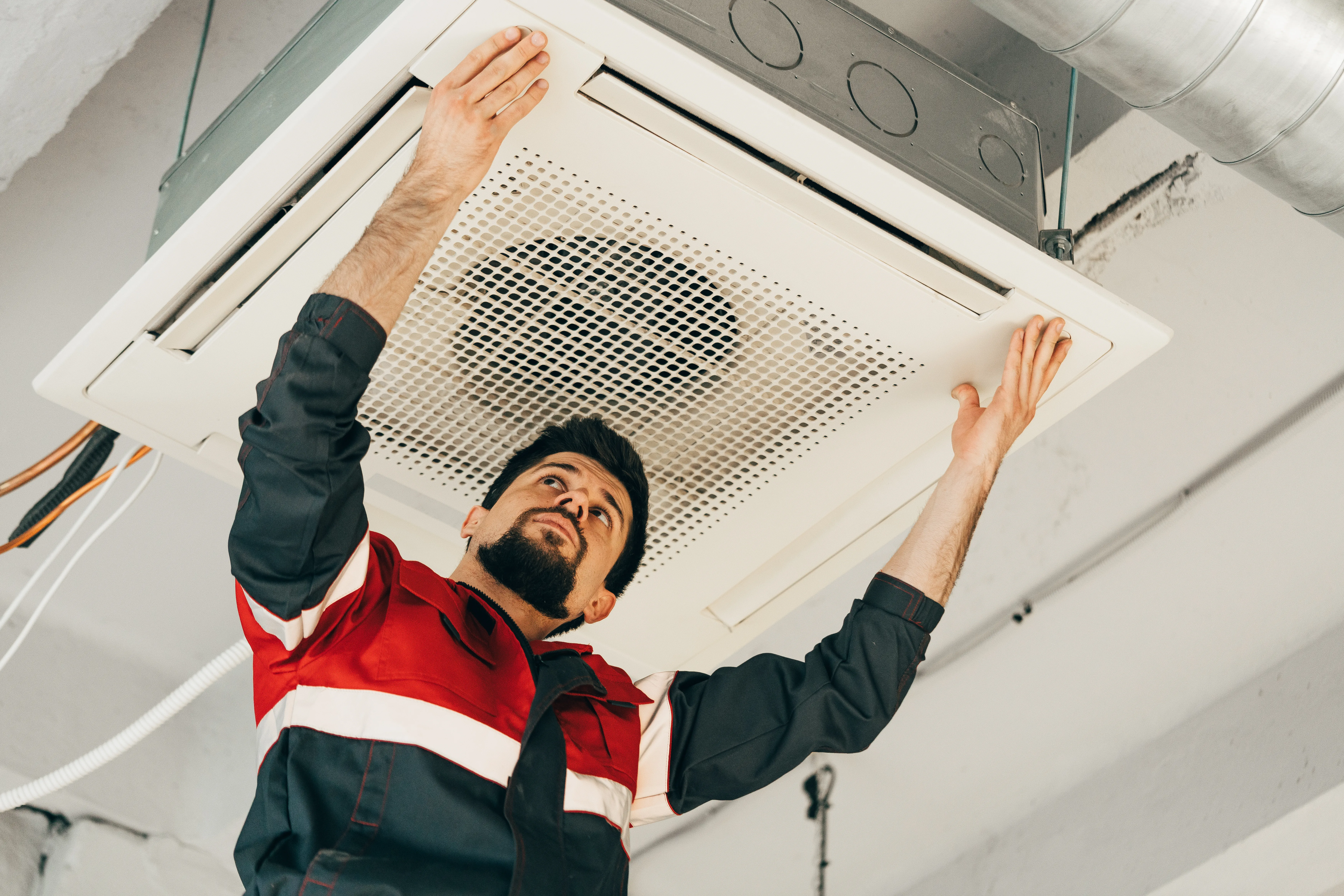 Un técnico da mantenimiento a una unidad de aire acondicionado de techo. La limpieza de los filtros de aire es parte de ello.