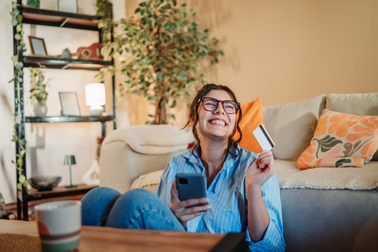 Joven feliz disfrutando de las compras online con tarjeta de crédito en el interior