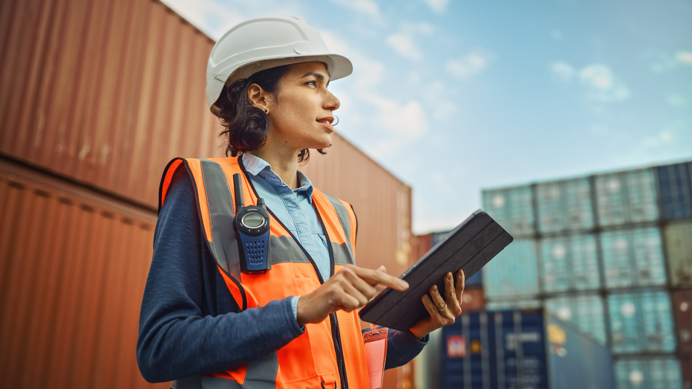 Retrato sonriente de una hermosa ingeniera industrial latina con sombrero duro blanco, chaleco de alta visibilidad que trabaj